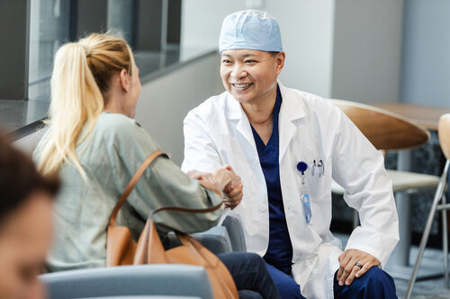 The unrecognizable woman thanks the smiling mature adult male emergency room surgeon for his efforts on behalf of her family member.