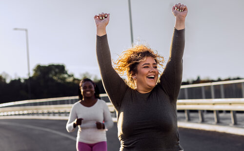 Two excited young plus size women jogging together.