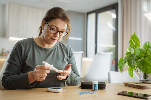 Mature diabetic woman using lancet on finger for checking blood sugar level by Glucose meter. 