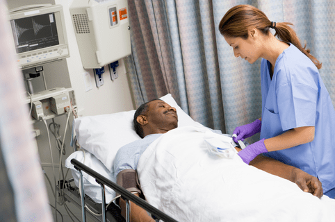 Nurse Caring For Patient In Hospital Bed Looking Down