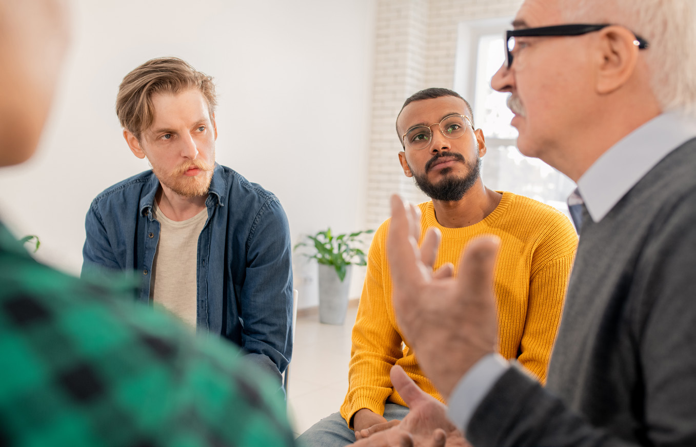 African American Man in a yellow sweater is listening attentively in a group setting