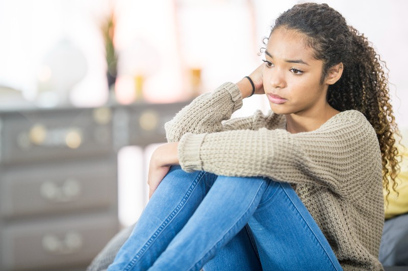 A teenage girl of African descent is indoors in a bedroom