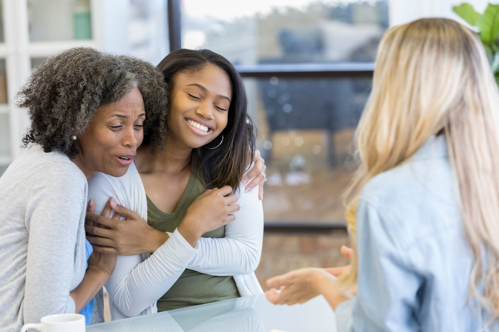 Smiling teen & mom hugging while speaking with healthcare worker