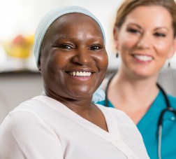 A nurse watches as a senior patient smiles, while in her home.