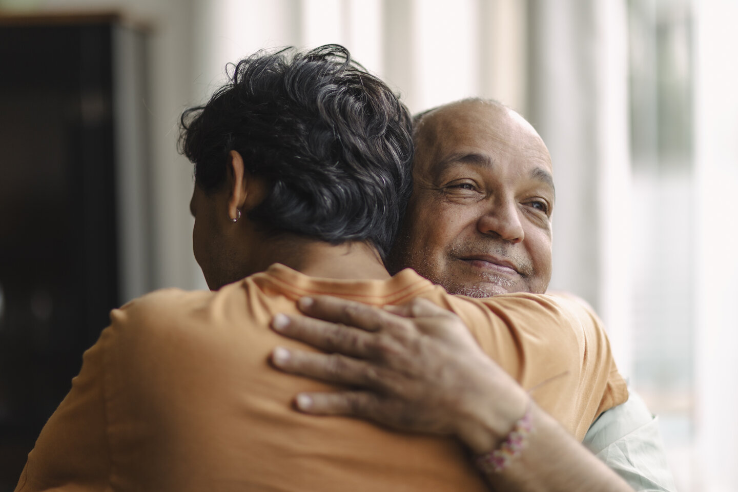 Two people hugging warmly, one smiling contentedly with eyes closed. The embrace conveys a sense of comfort, affection, and closeness.