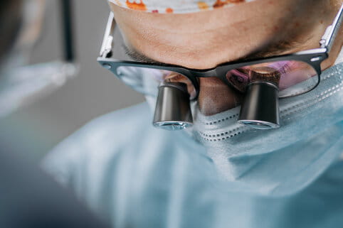 Close-up of a focused surgeon wearing magnifying glasses and a face mask, concentrating on a procedure in a sterile operating room.