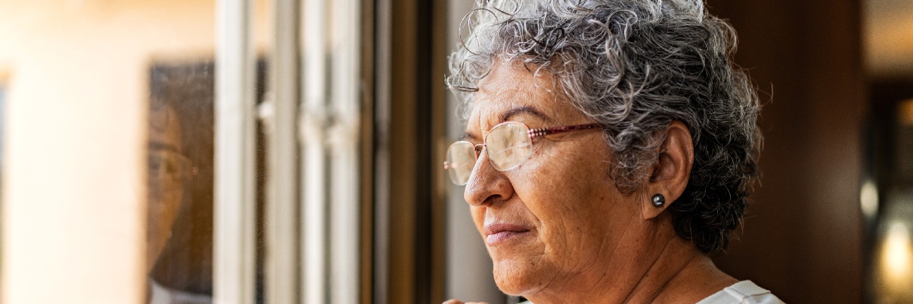 Older woman looking thoughtfully out a window, representing dementia awareness, memory care support, and neurological health services at Riverside Health.