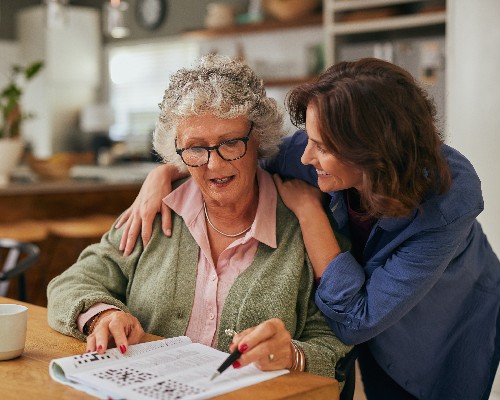 Senior woman solving crossword puzzle with the help of her daughter Neuro Spine Memory Care
