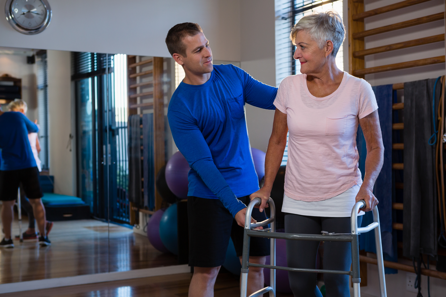 Physiotherapist assisting senior woman patient to walk with walking frame in clinic