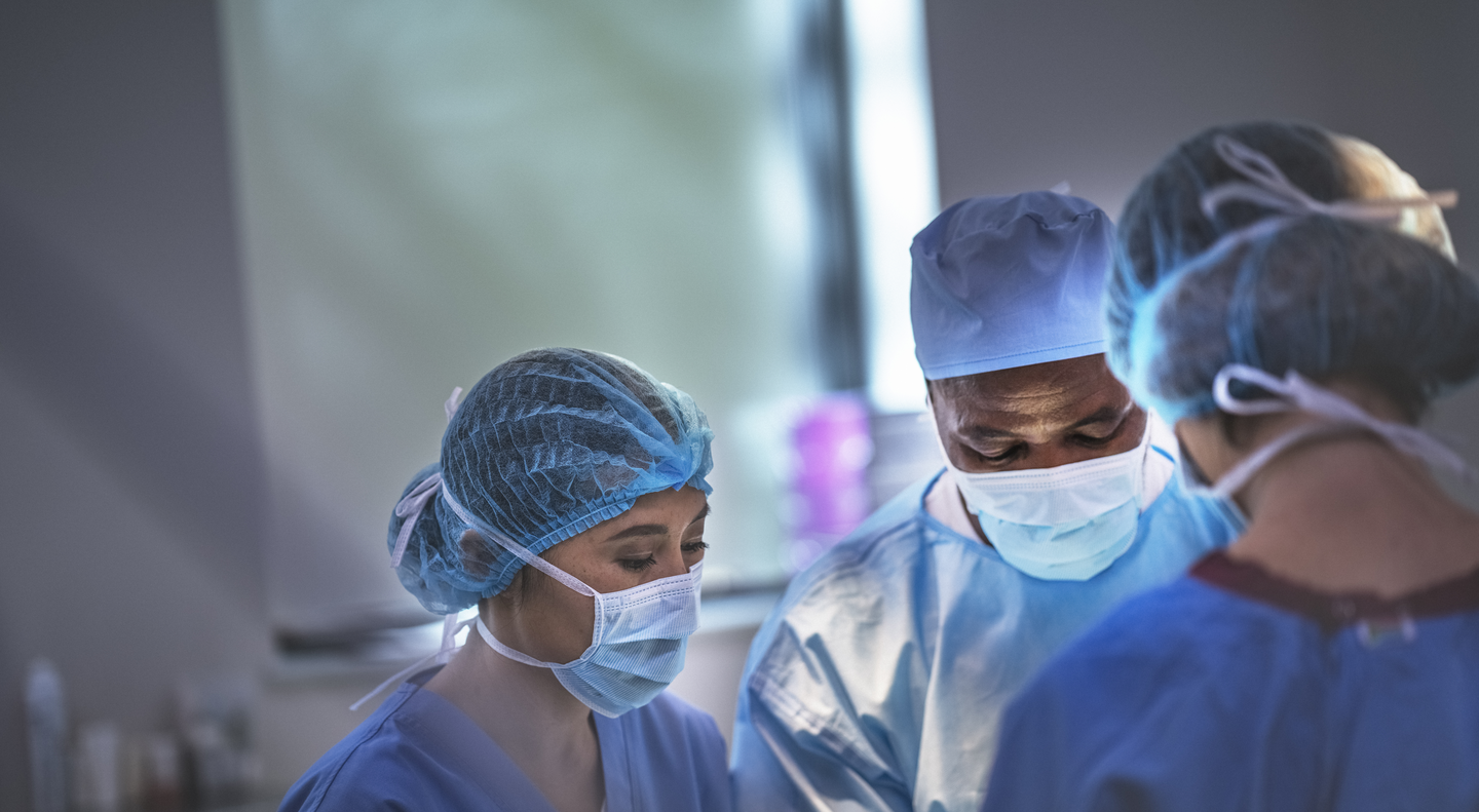 Multi-ethnic surgeons working at operating room at hospital. Team of doctors are standing in emergency room. They are wearing blue scrubs.
