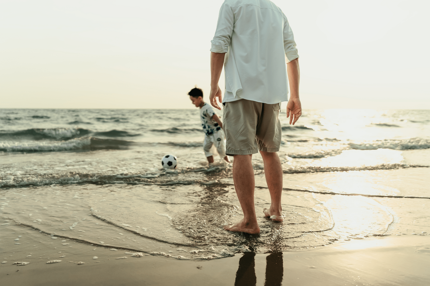 Father and son play football happily on the beach during vacation, travel, long weekend, summer or any other holiday. They are happy to spend time together.