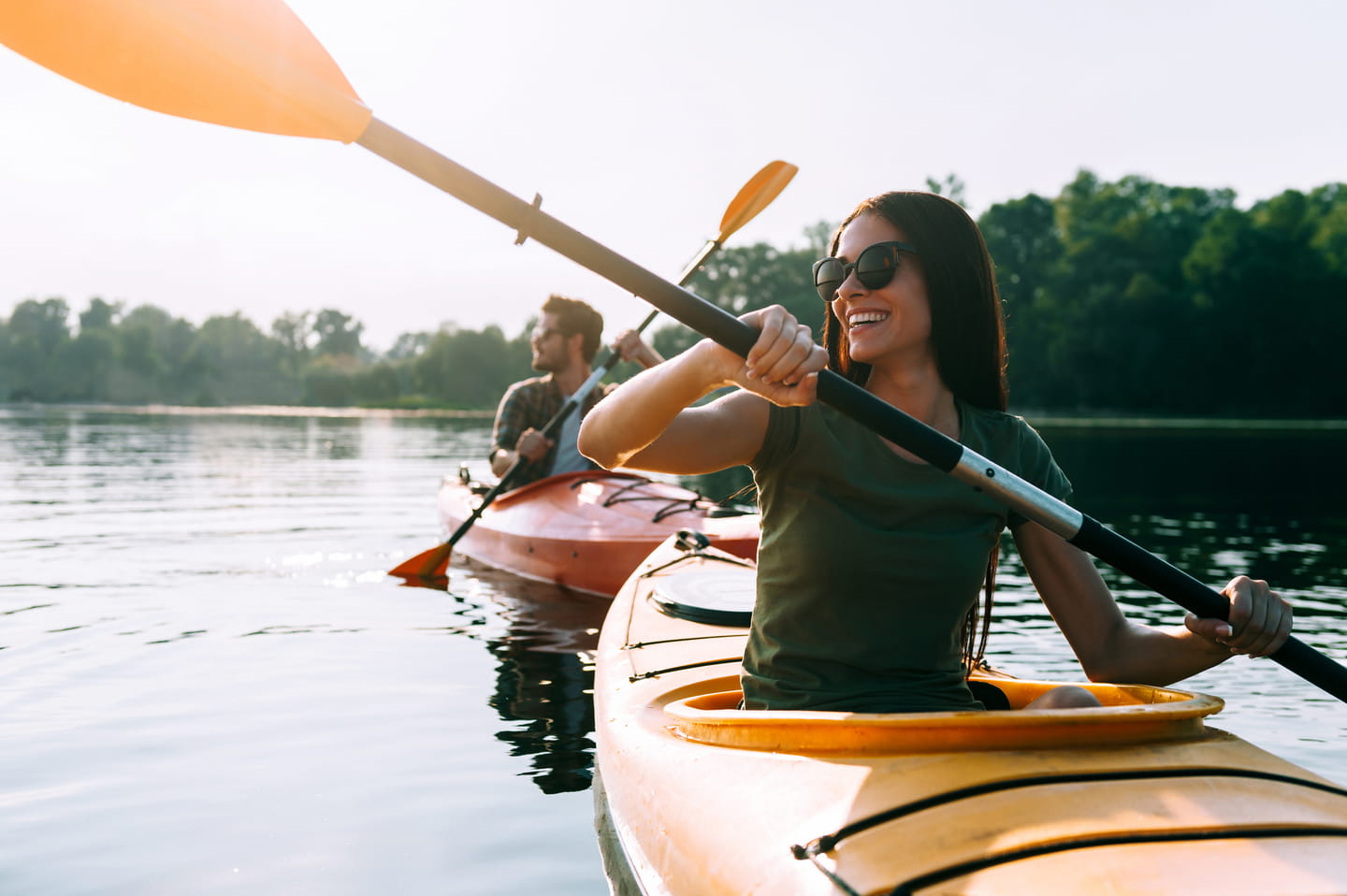 Two people kayaking on a calm river at sunset, smiling and paddling together.