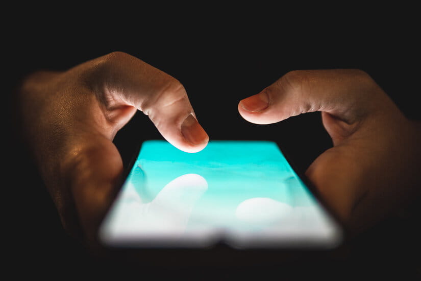 Two hands holding a smartphone with a glowing screen against a dark background, creating a tech-focused and immersive atmosphere.