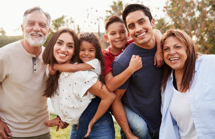 Primary Care Hereditary Risk Three generation Hispanic family standing in the park, smiling to camera