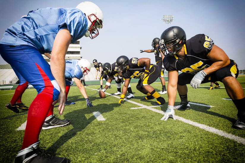 Players in black and yellow jerseys face off against players in blue and red jerseys on a football field, crouched in formation, ready to play.