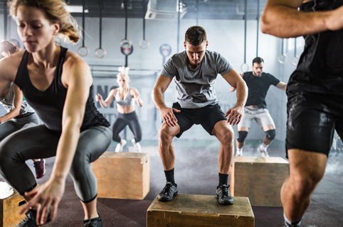 Large group of athletic people jumping on crates during cross training in a health club.