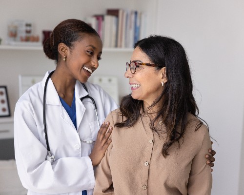 Female doctor gently touches shoulders, supporting elderly 60s patient