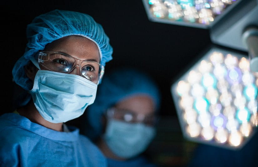 Hispanic medical doctor smiling at nurse in surgery operation room with colleagues and lights in hospital 