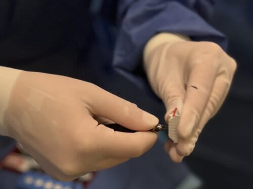 Two gloved hands are seen in a surgical setting, carefully holding medical equipment. The mood is precise and focused, emphasizing meticulous care.