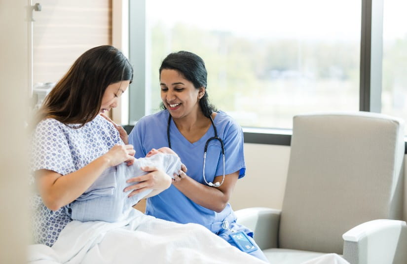 Female doctor sits bedside with the new mother to help answer her questions 
