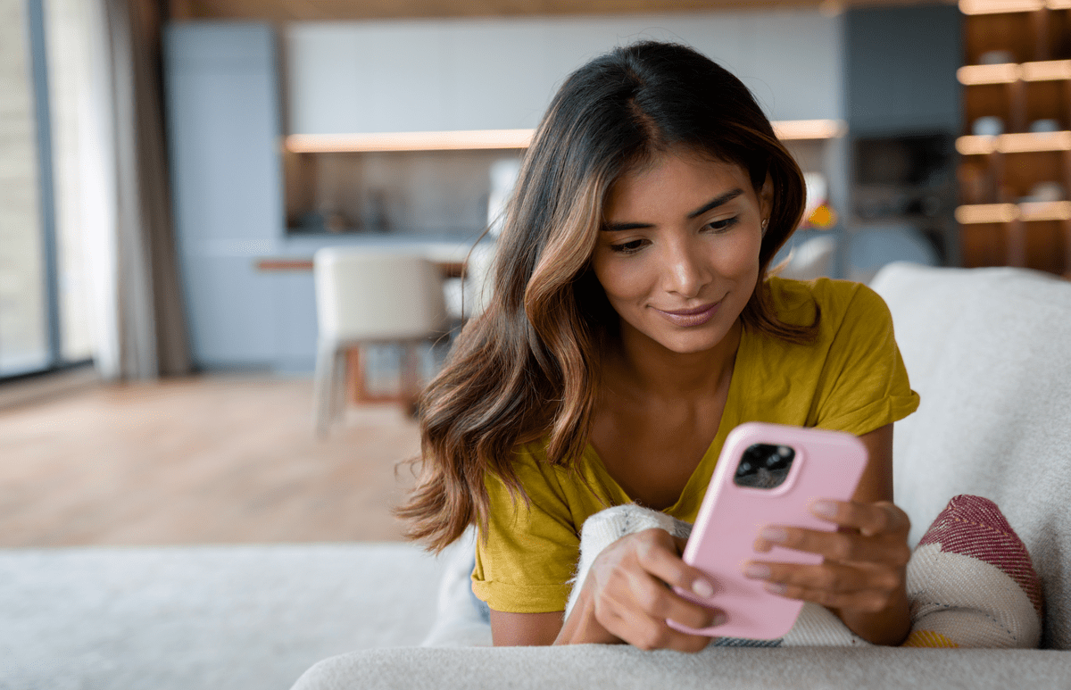 Woman at home lying on the couch looking at social media on her cell phone