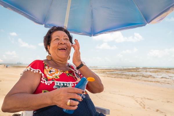 Woman sitting under an umbrella putting sunscreen on her face