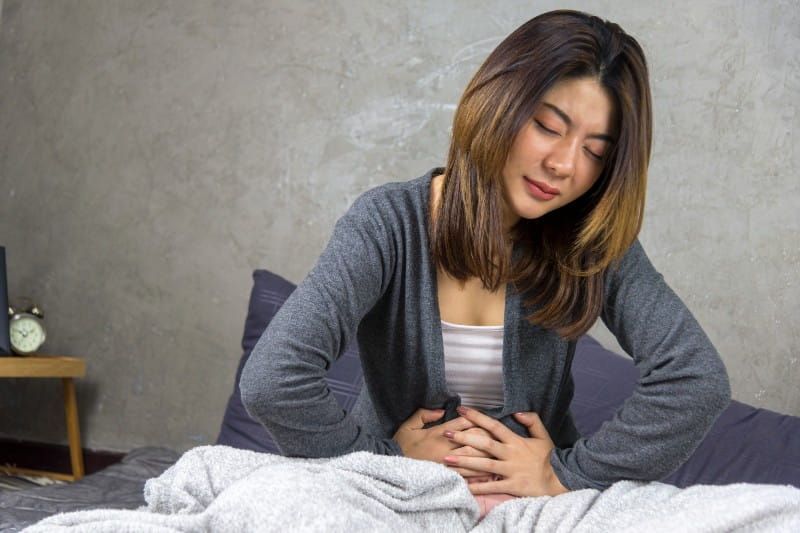 Woman sitting on Bed and feeling pain in her stomach
