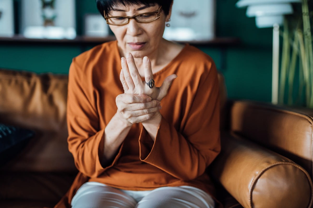 Senior Asian woman rubbing her hands in discomfort