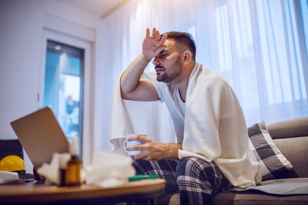 man holding his head at home sick