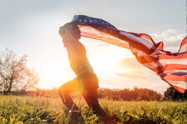 little boy running in a field with an American flag