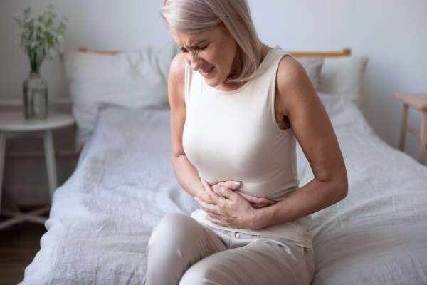 Woman holding her stomach sitting on her bed