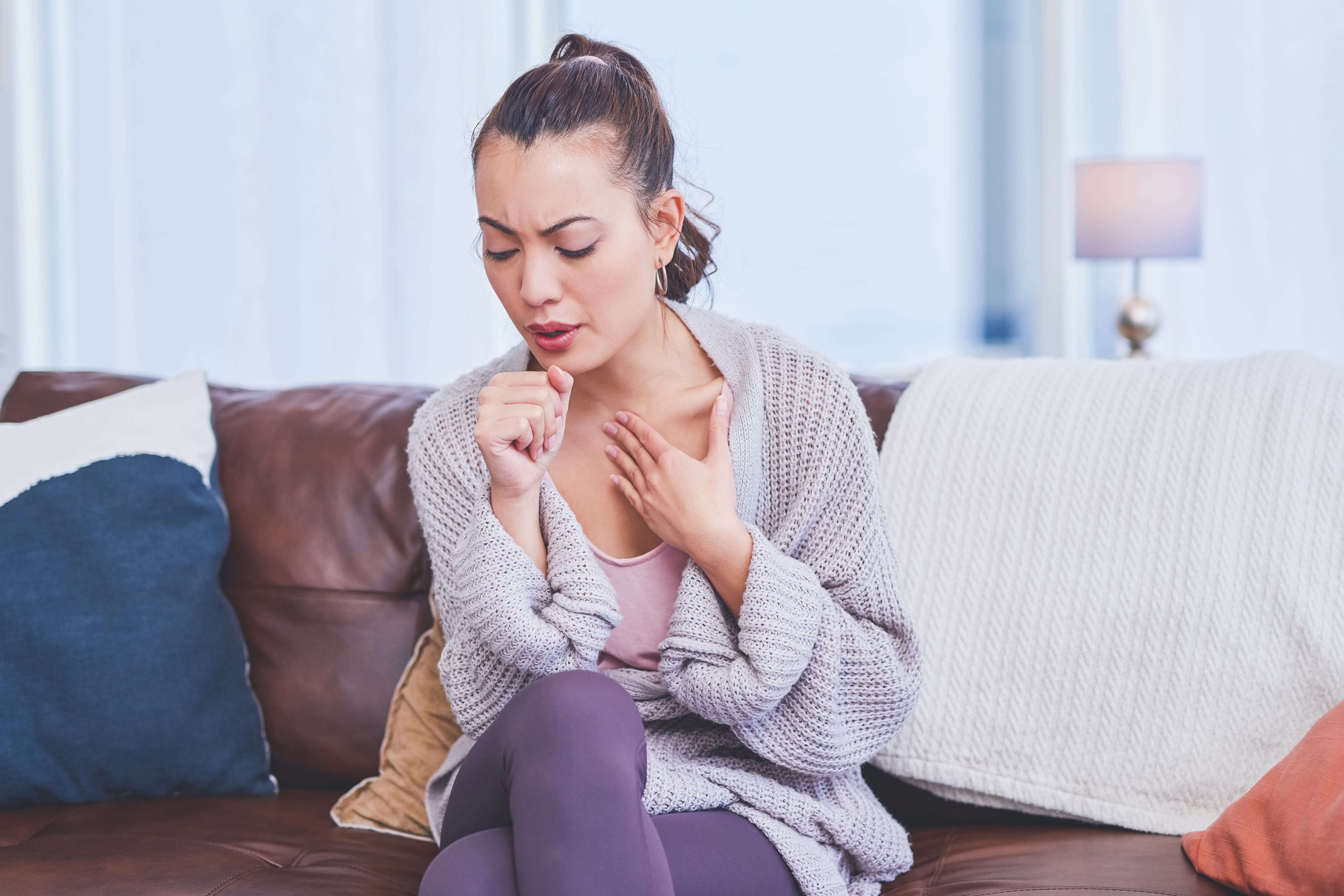 young woman sitting alone on her sofa at home and coughing