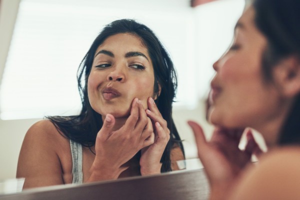 young woman looking at her skin in the mirror