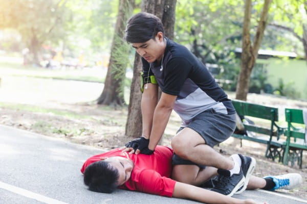 Asian man performing CPR on man in park
