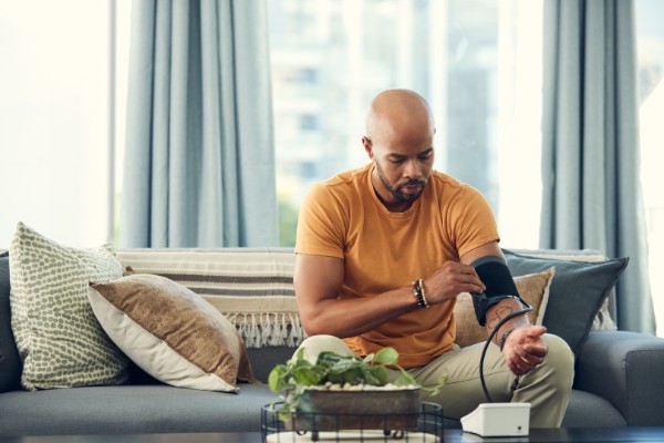 young man taking his blood pressure while sitting on the sofa at home