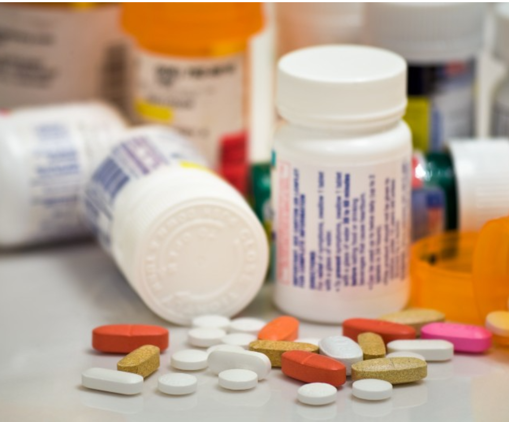A collection of assorted pills and tablets, red, white, and gold, scattered in the foreground. Blurred prescription bottles are visible in the background.