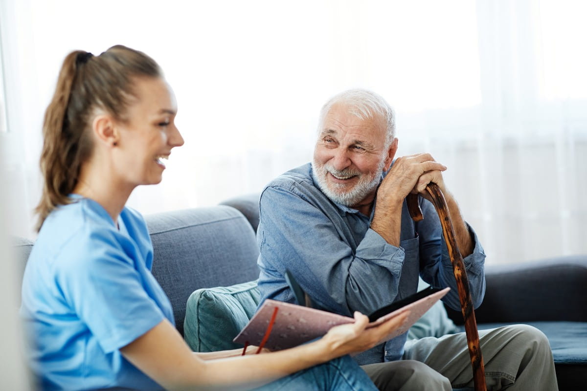 Doctor or nurse caregiver showing a brochure to senior man at home or nursing home