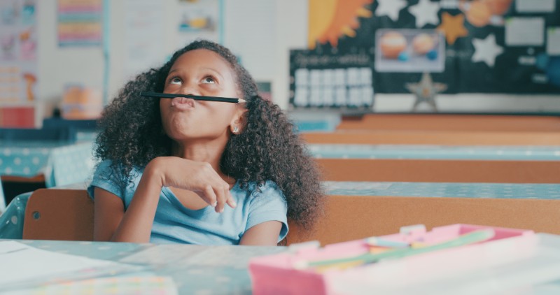 Shot of a young girl looking bored while playing at a school desk