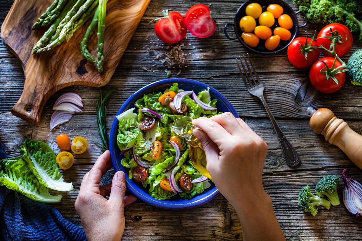 Dressing fresh organic vegetables salad with olive oil