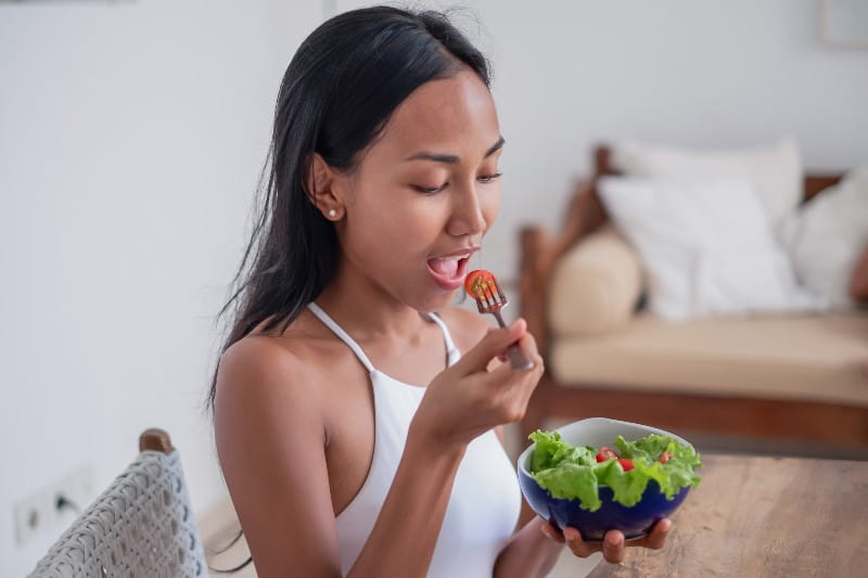 shot of a healthy Southeast Asian woman eating a bowl of vegetable salad for lunch.