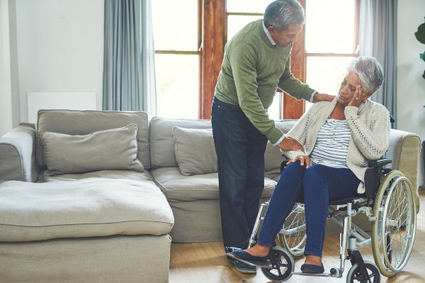 Shot of a worried looking elderly woman seated in a wheelchair while being supported and held by her husband