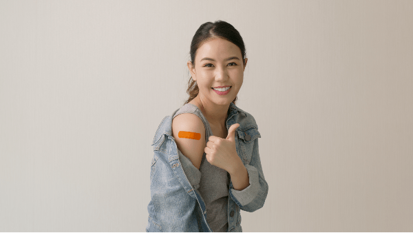 Asian woman smiling with a jean jacket off her shoulder with a bandaid on her upper arm 