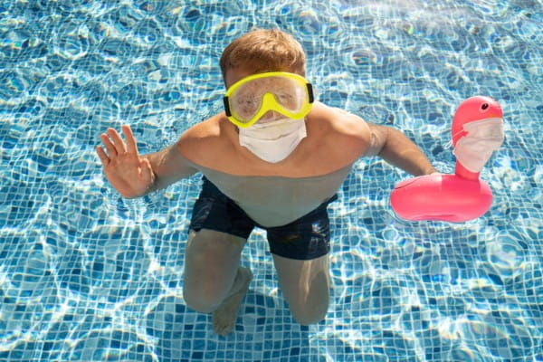 male in swimming pool with a toy flamingo in a medical face mask