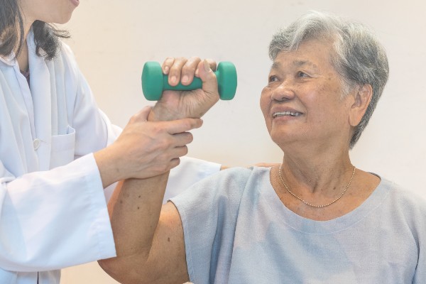 Senior elderly Asian woman with medical caregiver or physical therapist helping patient holding dumbbell
