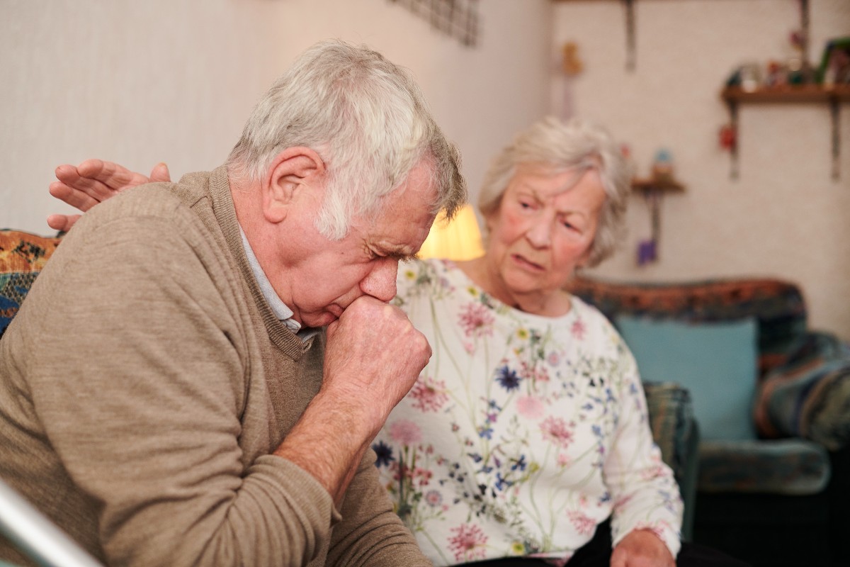 senior man with wife at home coughing badly