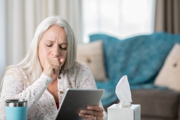 Woman coughing into hand while using tablet