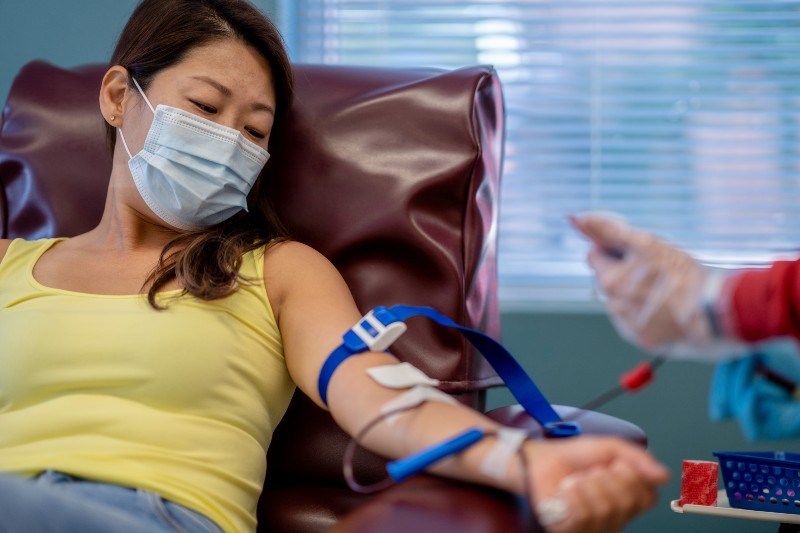 A masked Asian woman in her mid thirties is at a hospital for a blood donation drive.