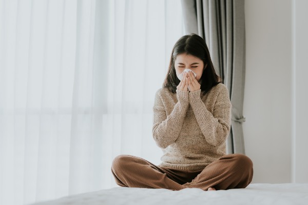 Sick Asian woman using a tissue to sneeze