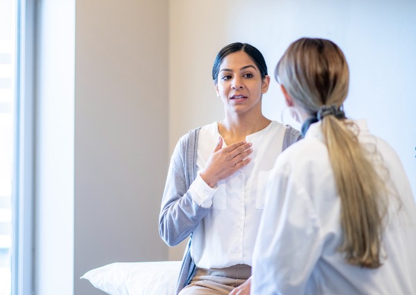 A middle-aged, mixed race woman, sits on an exam table in a doctors office 