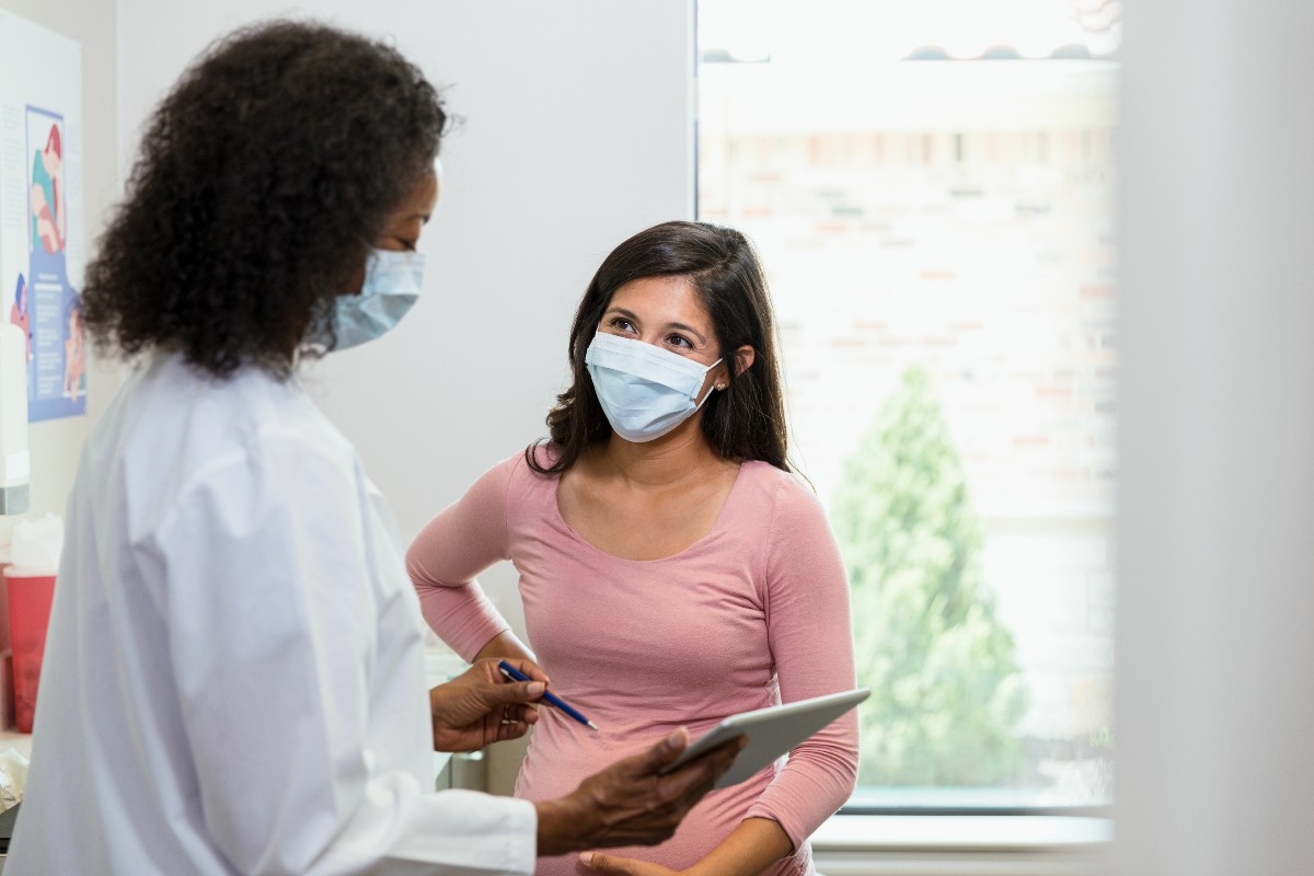 A mature adult doctor and her patient both wear masks to the consultation 